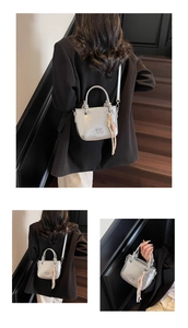 Detailansicht der silbernen Metallic-Eimertasche mit Logo und gewebtem Seilanhänger