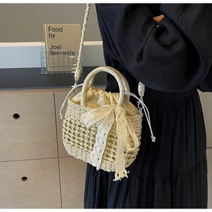 Détail du sac en paille tissé main avec un nœud en dentelle et des ornements dorés