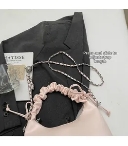 Pink pleated leather shoulder bag with adjustable chain strap on a grey blazer backdrop