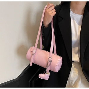 Close-up of pink cylinder shoulder bag with heart pendant on a stylish model outfit