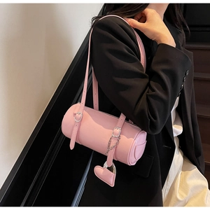 Detail of pink cylinder shoulder bag with heart pendant and silver buckles on black blazer
