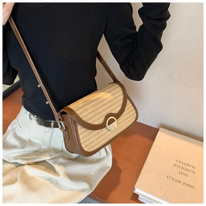 Gros plan d'un sac bandoulière en paille avec garniture en cuir brun et boucle métallique