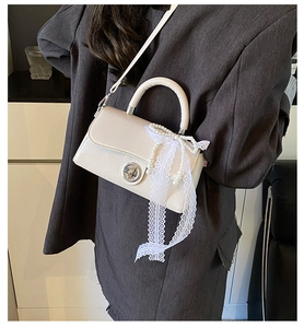 Detail of cream white PU handbag with lace bow, pearl charm, and metal twist-lock