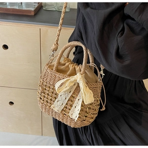 Détail du sac en paille avec grand nœud en dentelle crème et fermeture à cordon