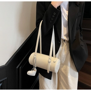 Model wearing a cream leather cylindrical Boston bag with a heart charm and strap