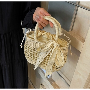 Gros plan d'un sac à main en paille beige avec un grand nœud en dentelle et doublure jaune