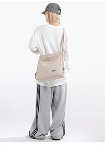 Rear view of model wearing a beige nylon messenger bag with adjustable wide strap