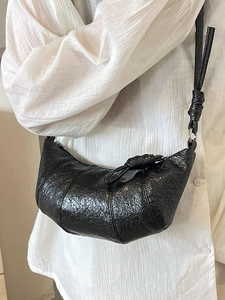 Sac à bandoulière noir brillant style croissant avec détails noués porté sur modèle