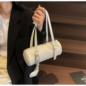 Detail of cream cilinder bag showing glossy leather texture and heart charm chain