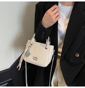Detail einer cremeweißen Leder-Eimertasche mit Metalllogo und buntem Web-Anhänger