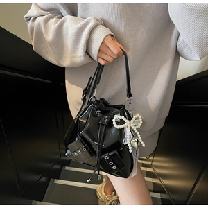 Détail du sac seau noir brillant avec nœud en perles et charms en dentelle sur la sangle