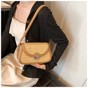 Détail du tissage en paille et du fermoir rond en métal sur le sac bandoulière marron
