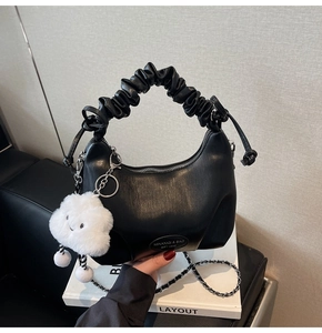 Detail of black pleated crescent bag with chain strap and fluffy cloud pendant