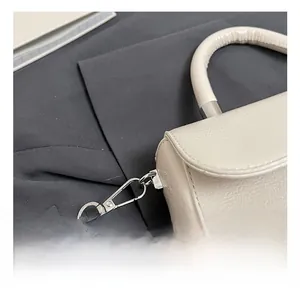 Detail view of silver metal hooks and pebble grain leather strap on a beige handbag