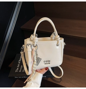 Detail der cremefarbenen PU-Beuteltasche mit Knotengriff und dekorativen Anhängern