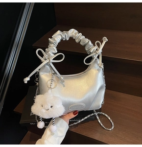 Detail of silver pleated hobo bag with cloud handle and plush charm on black props