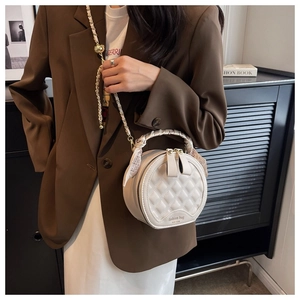 Gros plan d'un sac à main rond blanc matelassé avec poignée en foulard de soie et chaîne dorée