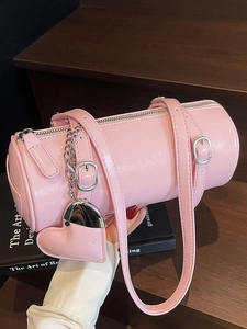 Pink oil wax leather cylinder bag with heart mirror charm held on dark wood stairs