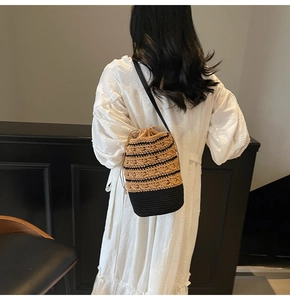 Detail of woven straw bucket bag with drawstring closure and slim black crossbody strap
