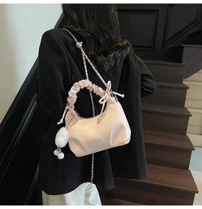 Detail view of pink pleated handbag with metal chain and white fluffy pom pom charm