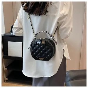 Détail d'un sac rond noir matelassé avec poignée en soie et bandoulière en chaîne