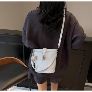 Dettaglio di una borsa a secchiello in pelle bianca con ciondolo a perla e fiocco