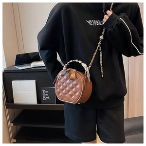 Détail d'un sac rond marron matelassé avec bandoulière chaîne et poignée en foulard