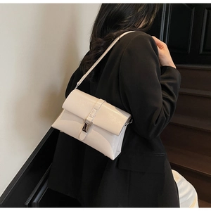 Close-up of off-white faux leather shoulder bag with silver buckle worn by a model