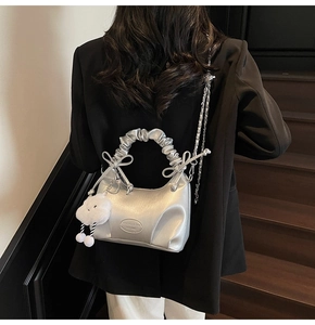Detail of silver metallic pleated handbag with bow accents and plush cloud charm pendant