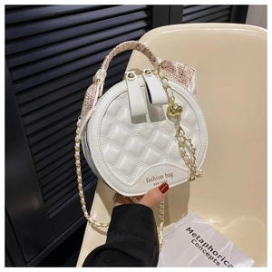 Close-up of quilted white round handbag with silk-wrapped handle and gold chain detail