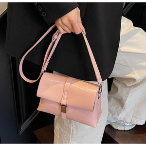 Close-up of pink glossy oil wax leather handbag with metal buckle worn with black blazer