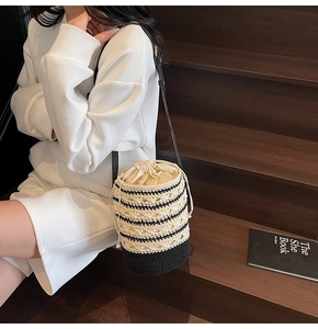 Close-up of black and white striped woven bucket bag with cream drawstring and leather strap