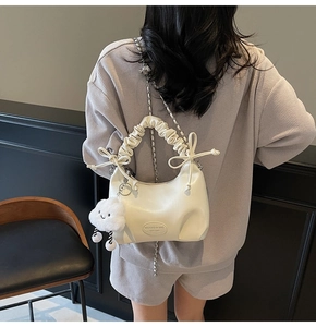 Detail of cream pleated handbag with bow accents and cute cloud charm on a model
