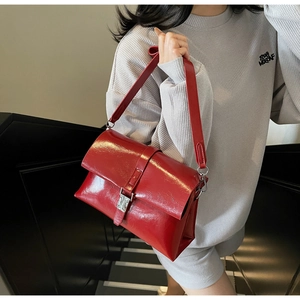 Detail of red glossy shoulder bag with silver metallic buckle and adjustable strap