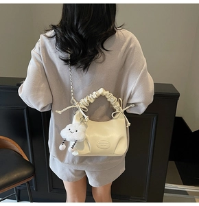 Detail of white pleated handbag featuring a plush cloud charm and silver chain strap