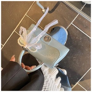 Close-up of light blue mini square bag featuring lace ribbon and elegant pearl handle detail