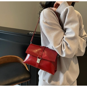 Detail of red wax leather underarm bag with silver metallic buckle on a grey sweater