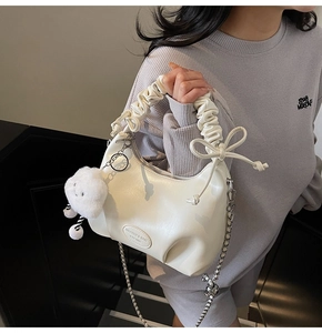Detail shot of a cream white ruched handbag with a cute plush cloud pendant and chain strap