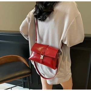 Red glossy oil wax leather underarm bag with silver buckle worn by a model in gray
