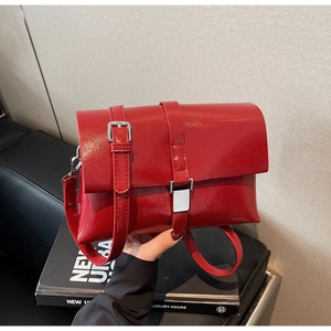 Detail view of the red glossy faux leather finish with silver metal buckles on the bag