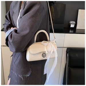 Detail showing creamy white glossy handbag with large lace bow and pearl chain decoration