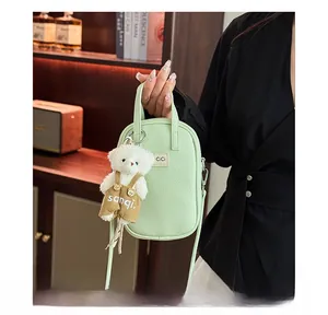 Détail d'un sac à bandoulière vert clair texturé litchi avec un pendentif d'ours mignon