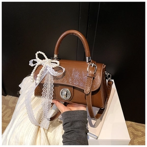Detail of brown patent leather handbag featuring lace pearl bow charm and silver lock