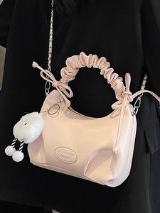 Pink pleated dumpling bag with silver chain strap and white plush charm on black suit