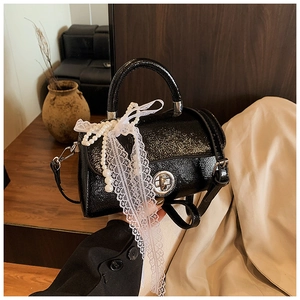 Detail of glossy black patent leather bag with white lace bow and pearl chain