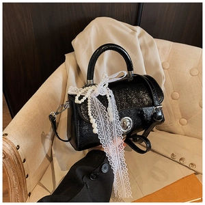 Detail of black glossy faux leather handbag with pearl chain and white lace bow decoration