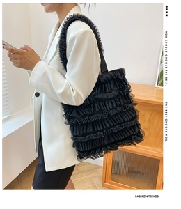 Détail du sac cabas en maille noire à volants porté par un mannequin en blazer blanc