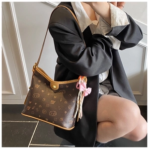 Detalle de un bolso de hombro marrón con estampados y colgante de lazo rosa decorativo