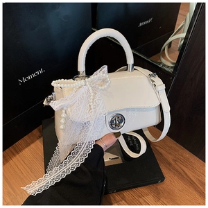 Close-up of white patent leather handbag with oversized lace bow and pearl chain detail