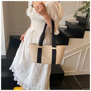 Primer plano del bolso tote trenzado beige con asas negras llevado por una modelo